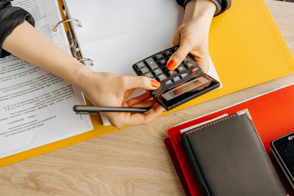 pexels-photo-8296974-8296974 Hands using a calculator at a desk with documents and folders, ideal for finance or accounting themes.